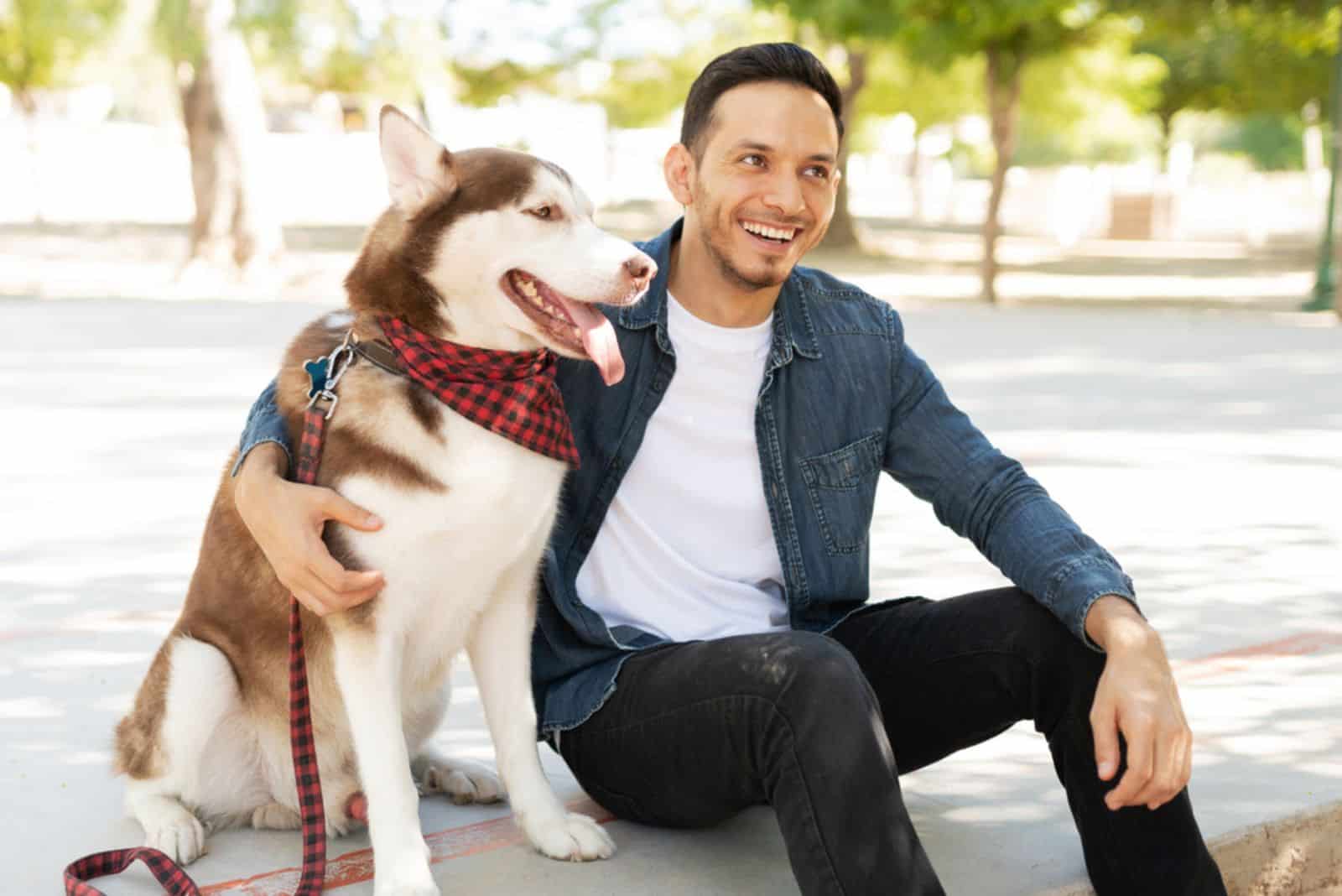 Atractivo dueño de perro riendo y abrazando a un hermoso husky