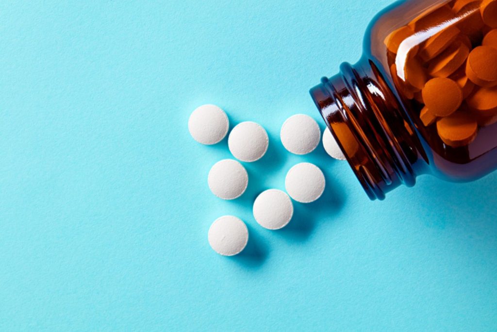 Píldoras y tabletas médicas blancas derramándose de una botella de medicamento