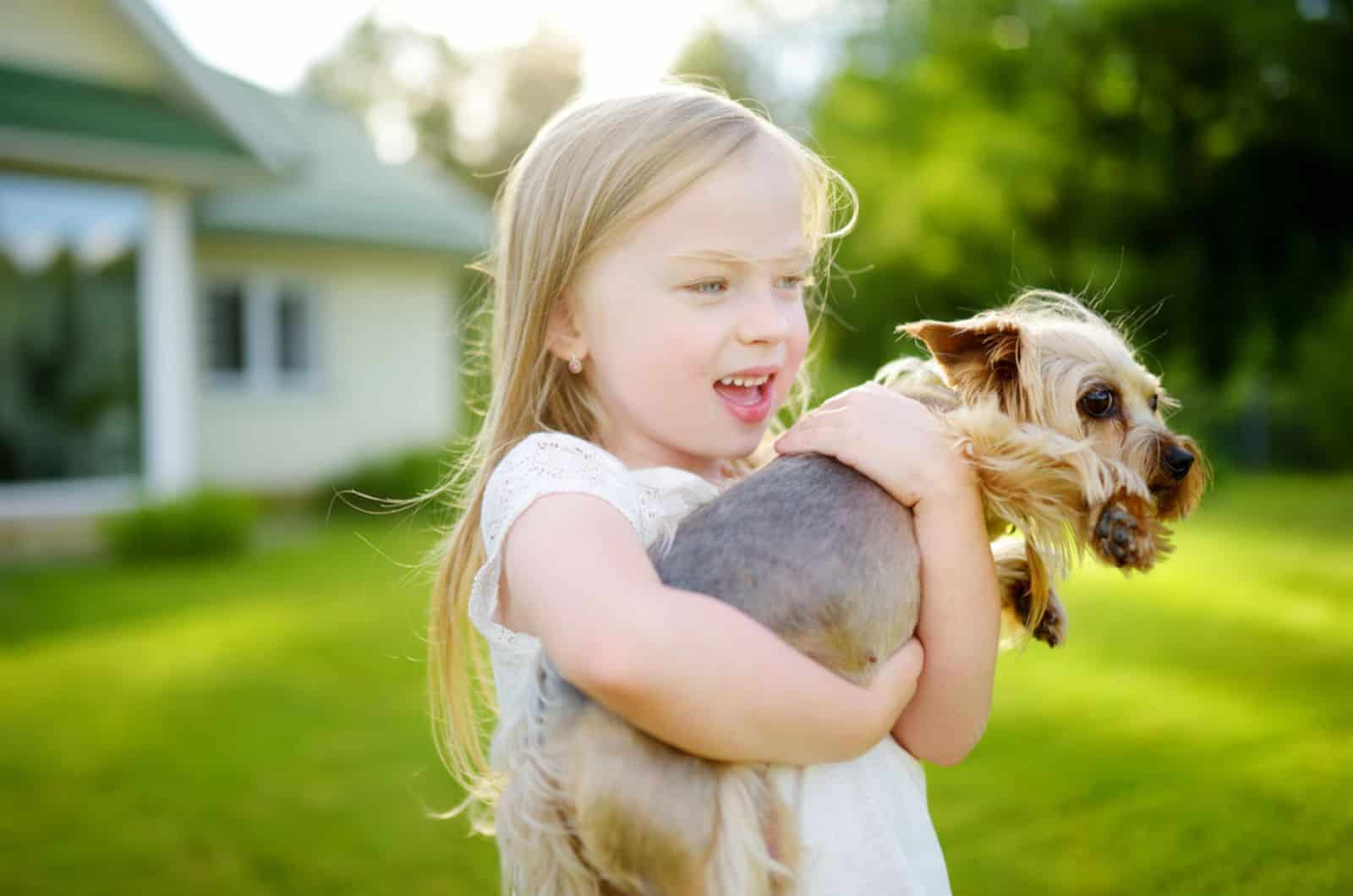 una niña pequeña sosteniendo su perro yorkshire terrier en el patio