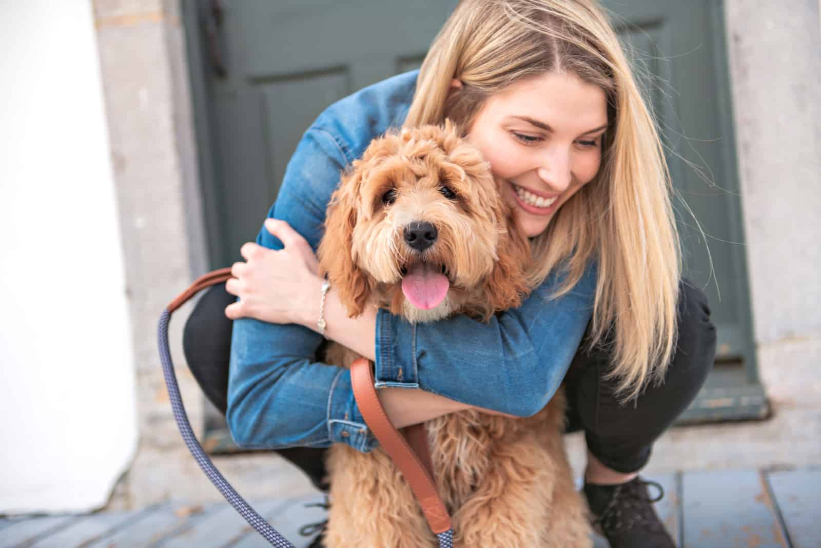 una rubia sonriente abraza un labradoodle afuera