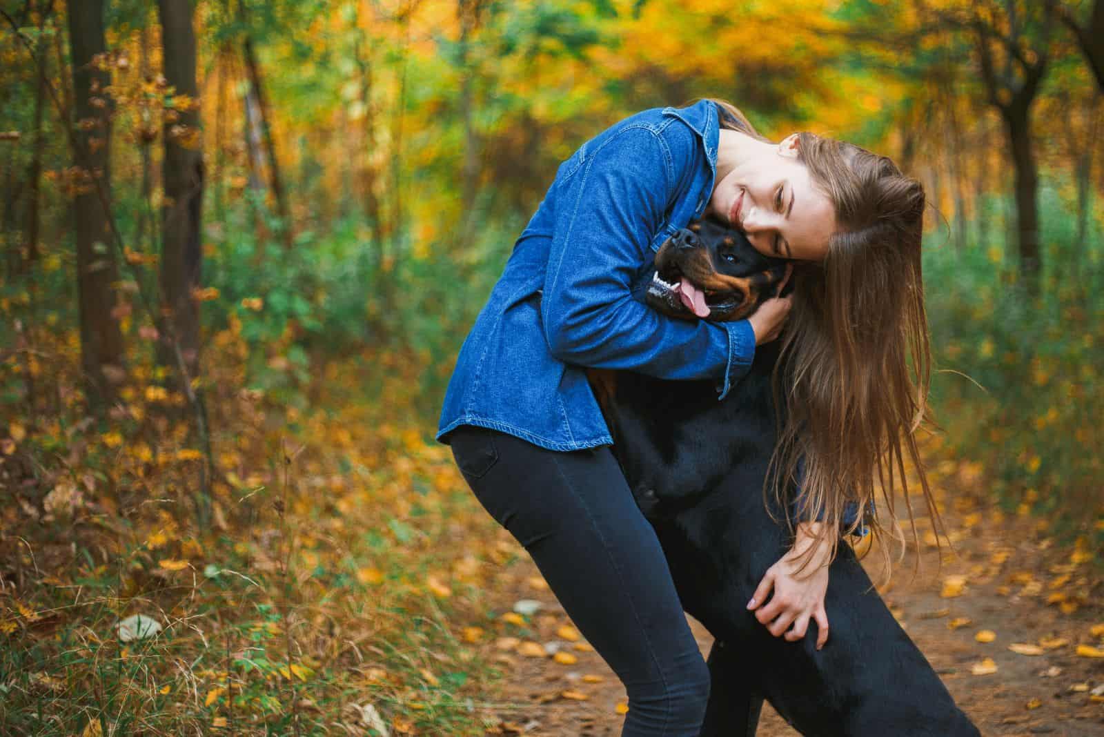 una mujer con un Rottweiler acurrucándose en el bosque
