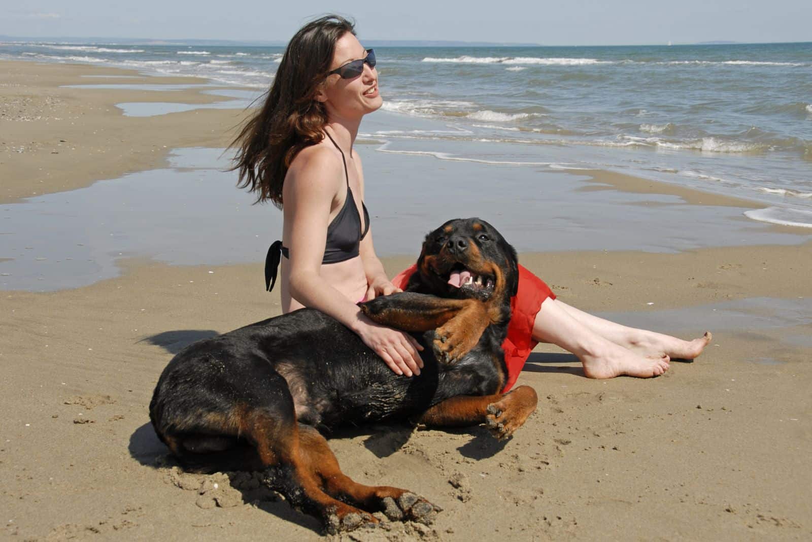 una mujer con un Rottweiler disfruta de la playa