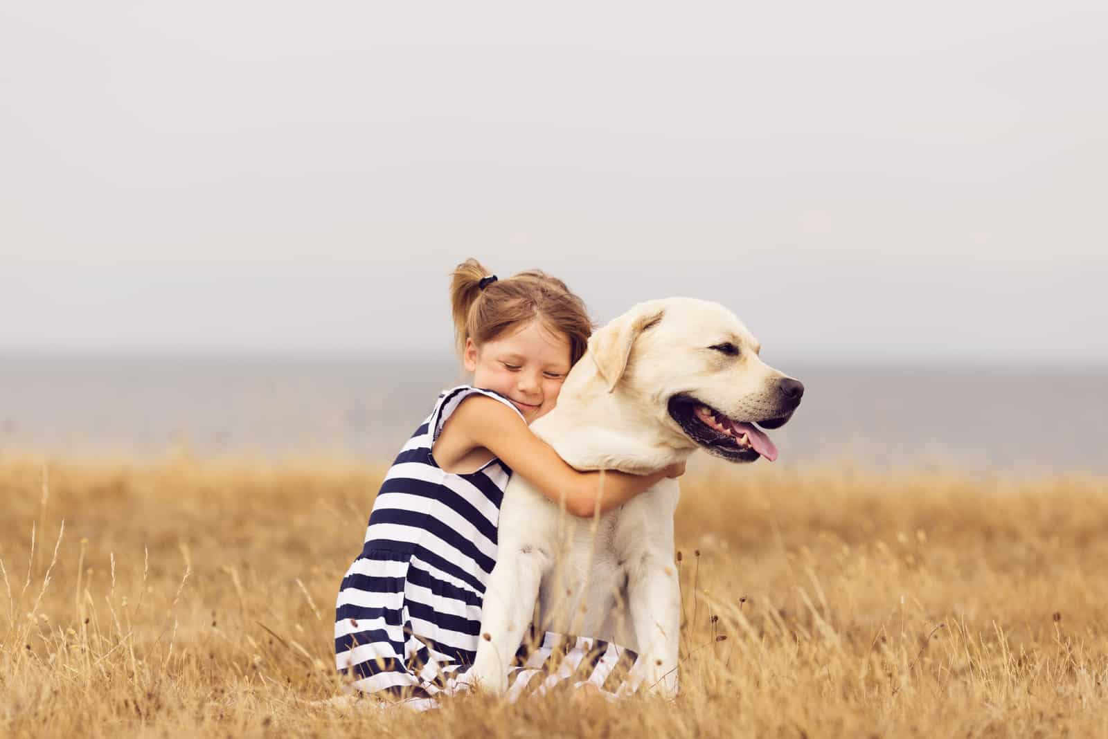 niña pequeña abrazando a un labrador retriever
