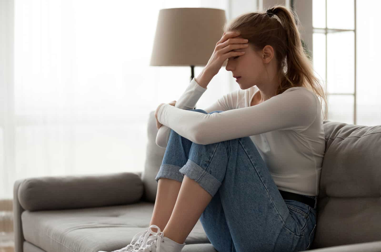 mujer triste sentada encogida en el sofá