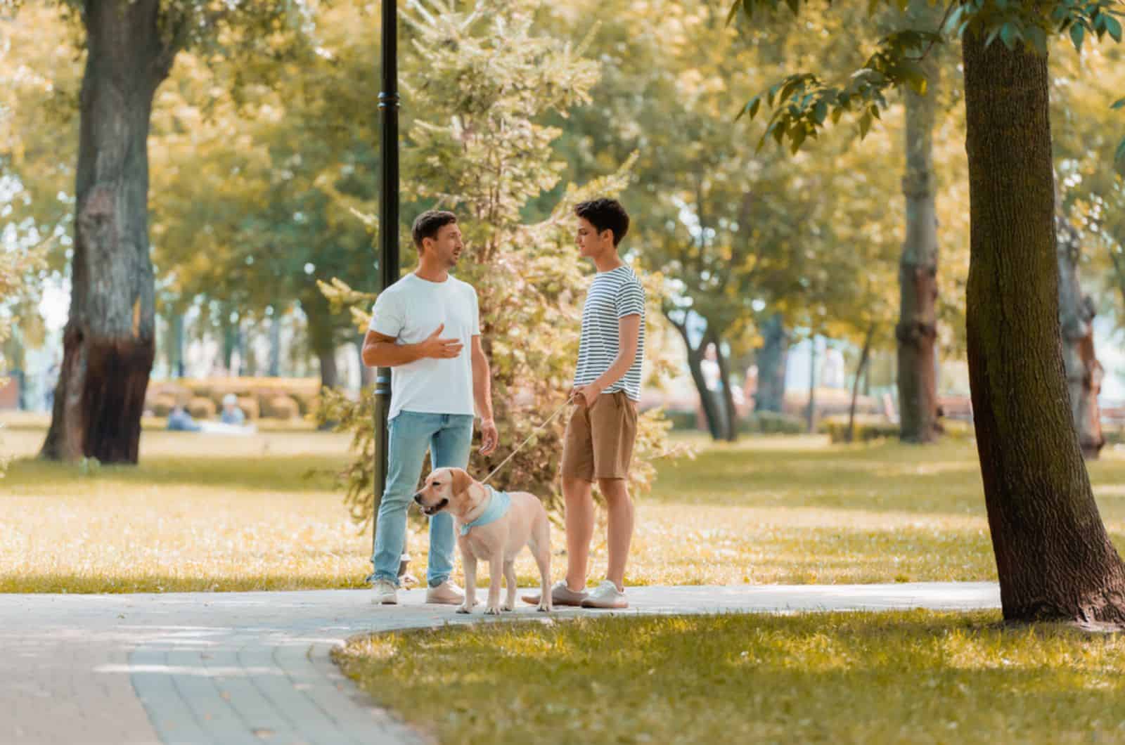 dos hombres hablando en el parque mientras pasean con el perro