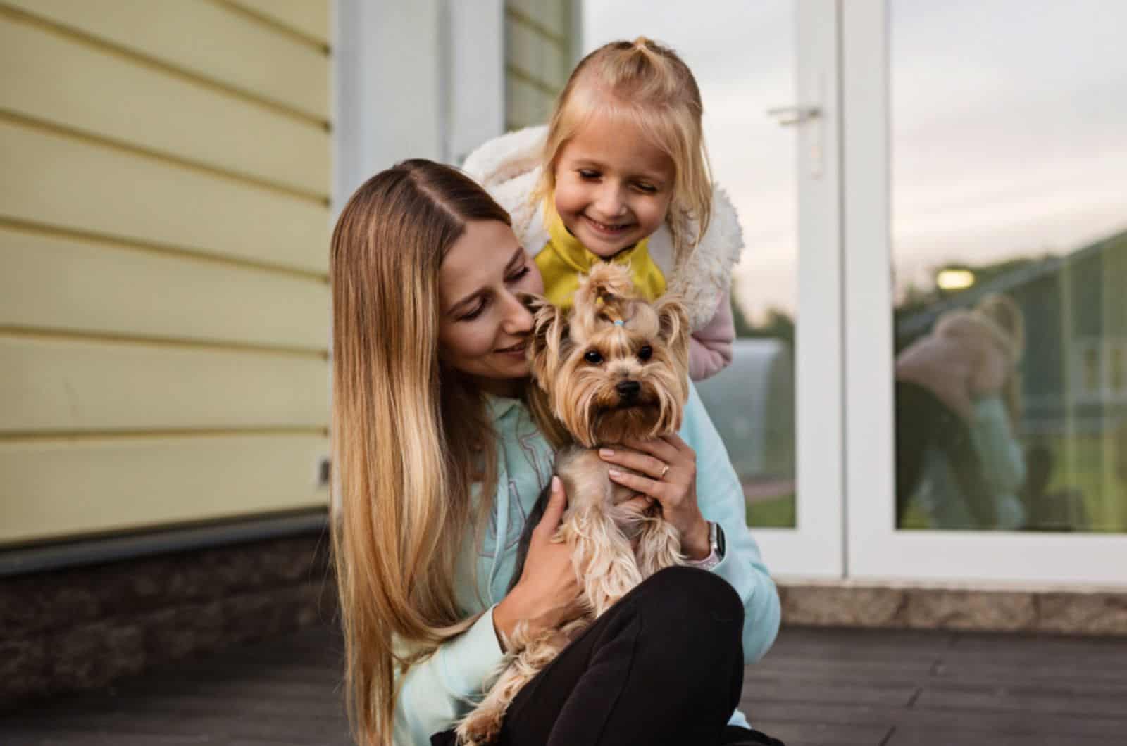 mujer sosteniendo un pequeño perro yorkshire terrier junto a una niña sentada