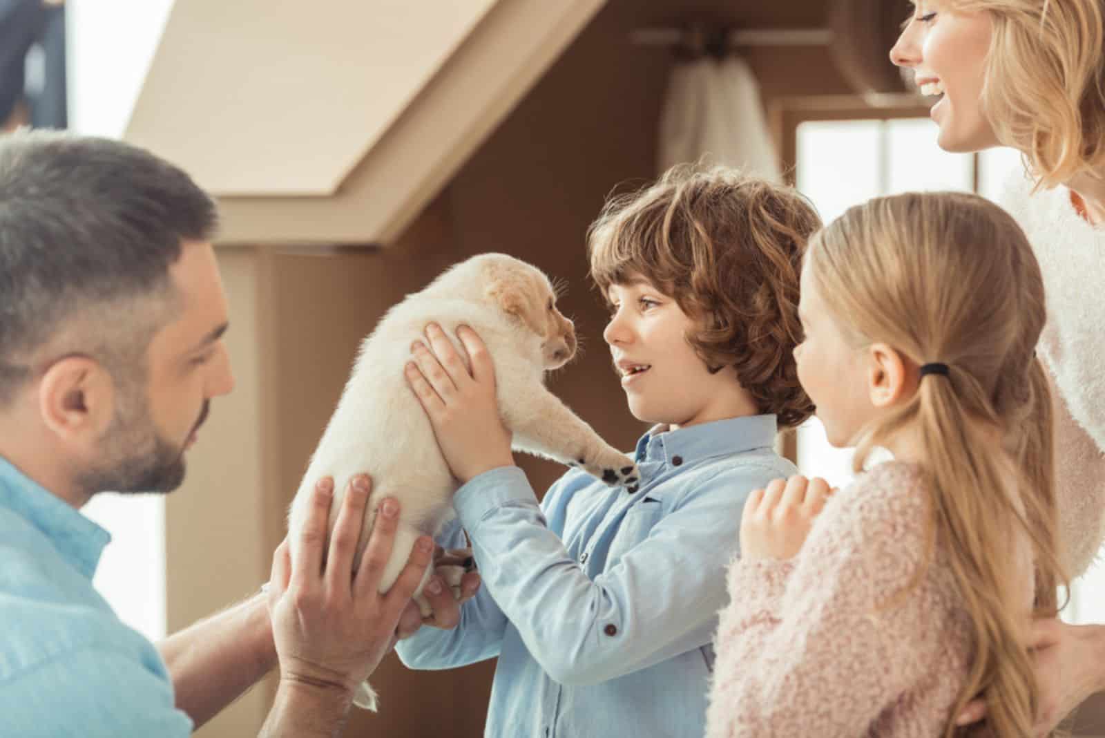 familia joven con un pequeño cachorro de labrador frente a una casa de cartón