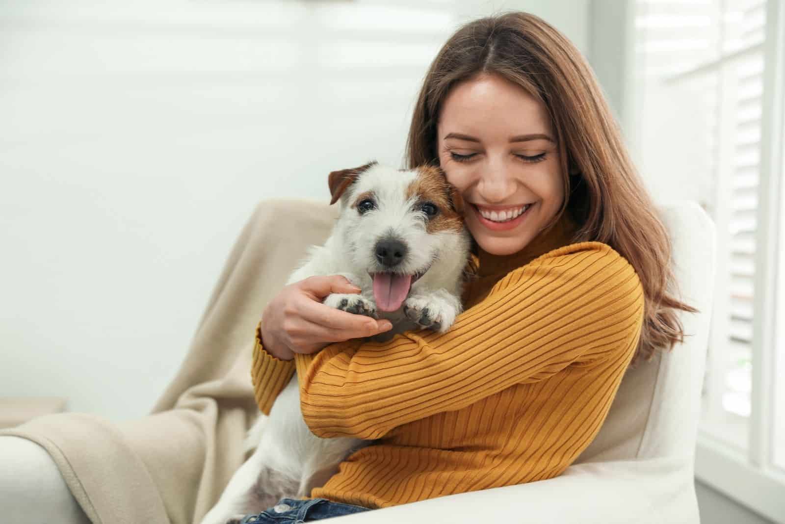 mujer joven abrazando un perro y sentada en el sofá