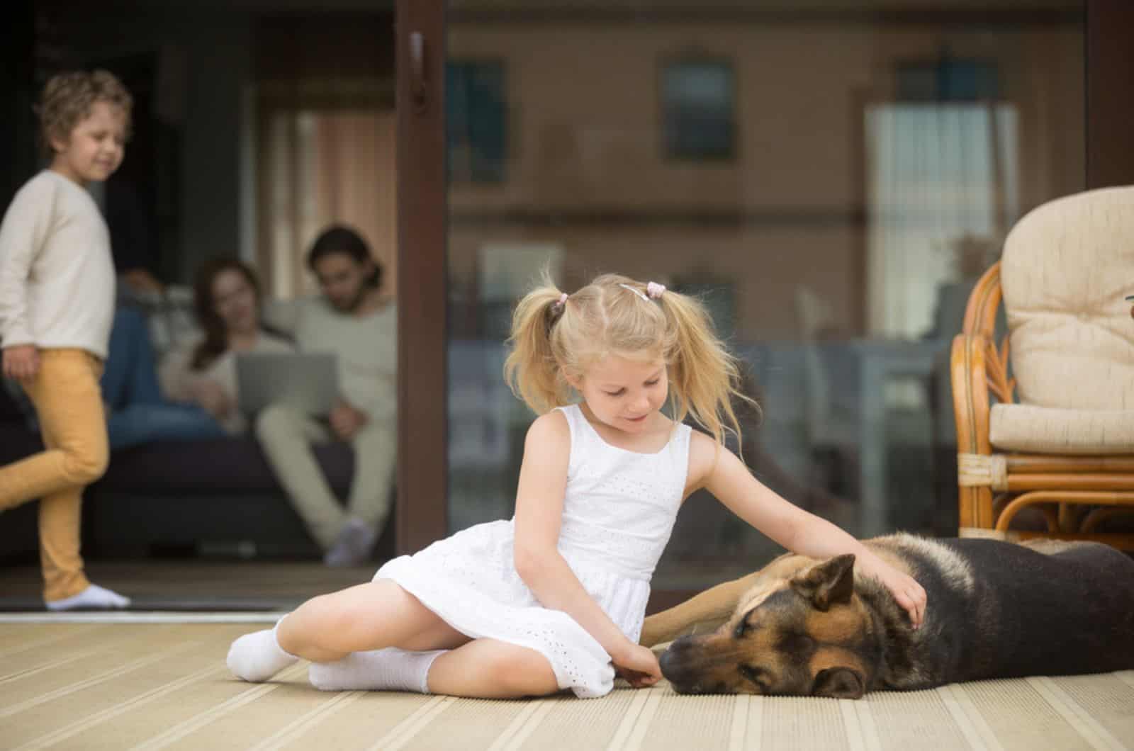 niña pequeña jugando con perro pastor alemán tumbado en el porche