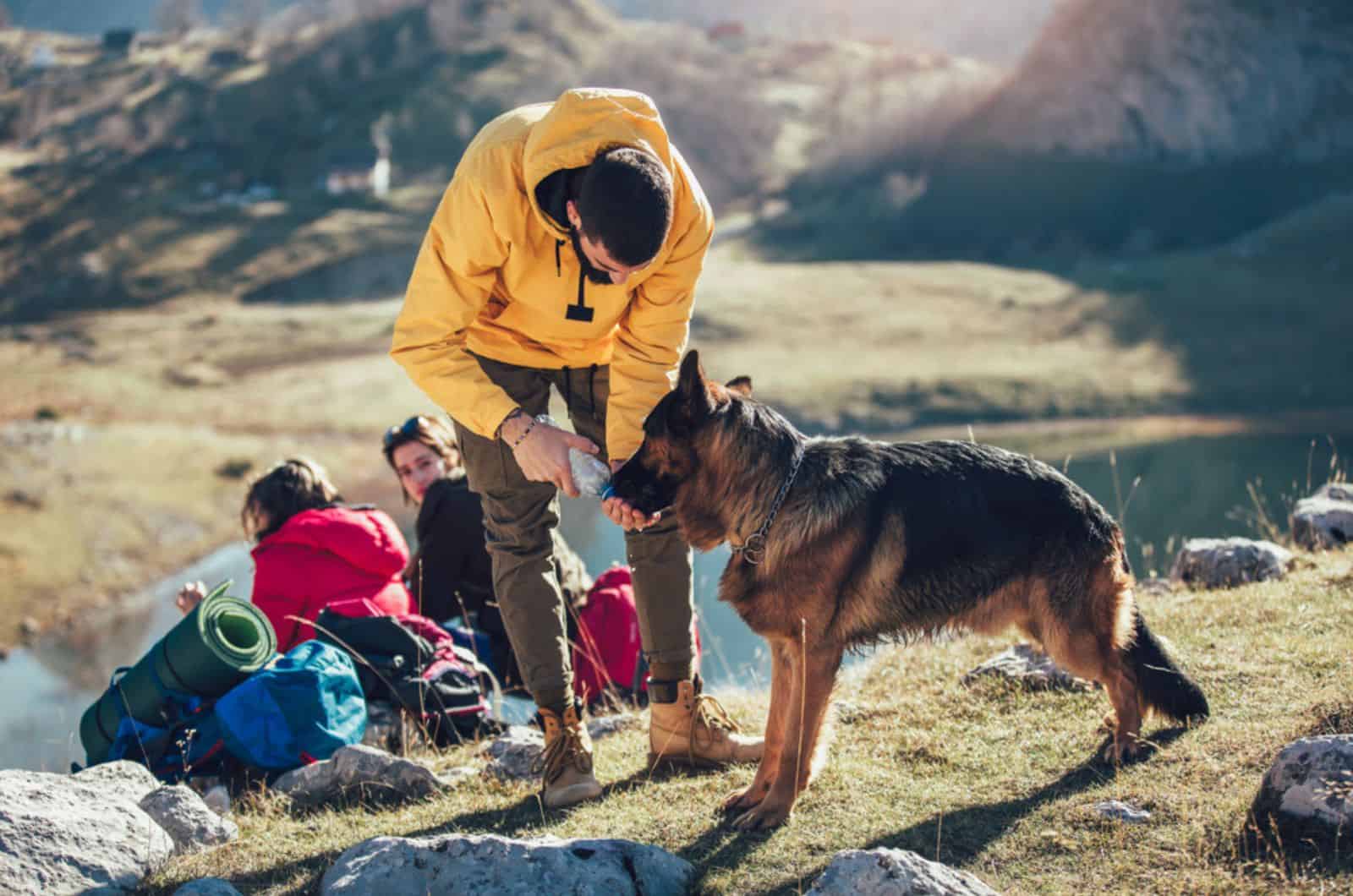hombre da agua al perro mientras descansa del senderismo