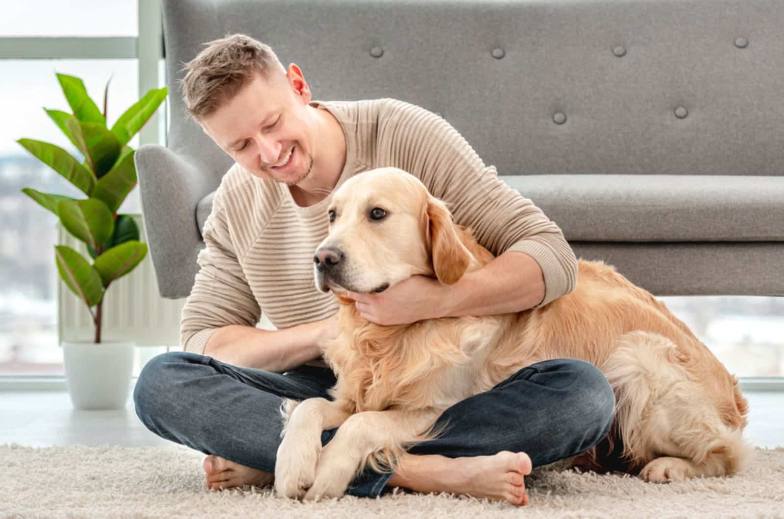 hombre abrazando a un perro golden retriever mientras está sentado en el suelo