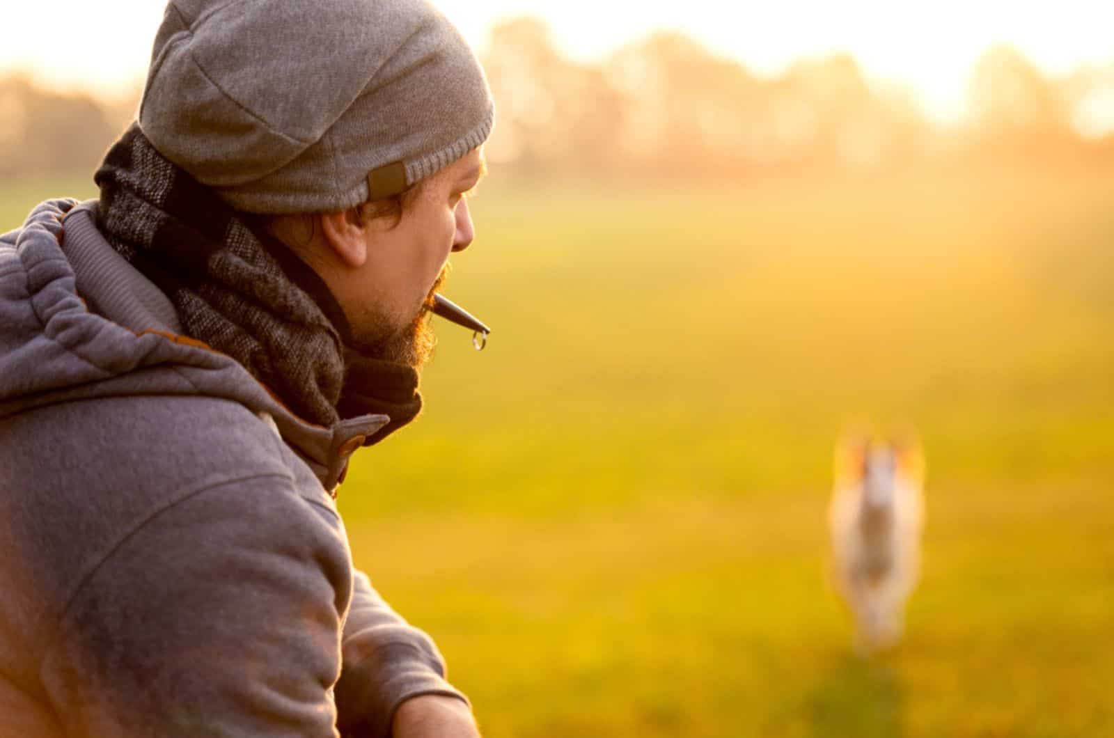hombre recordando a su perro con un silbato de perro durante el entrenamiento
