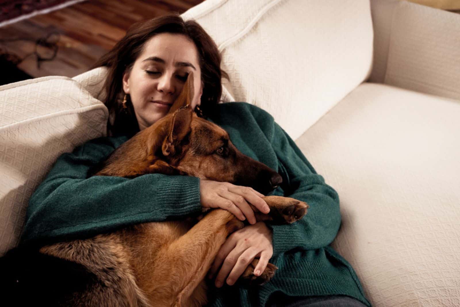 mujer sonriendo acurrucándose con su perro en el sofá