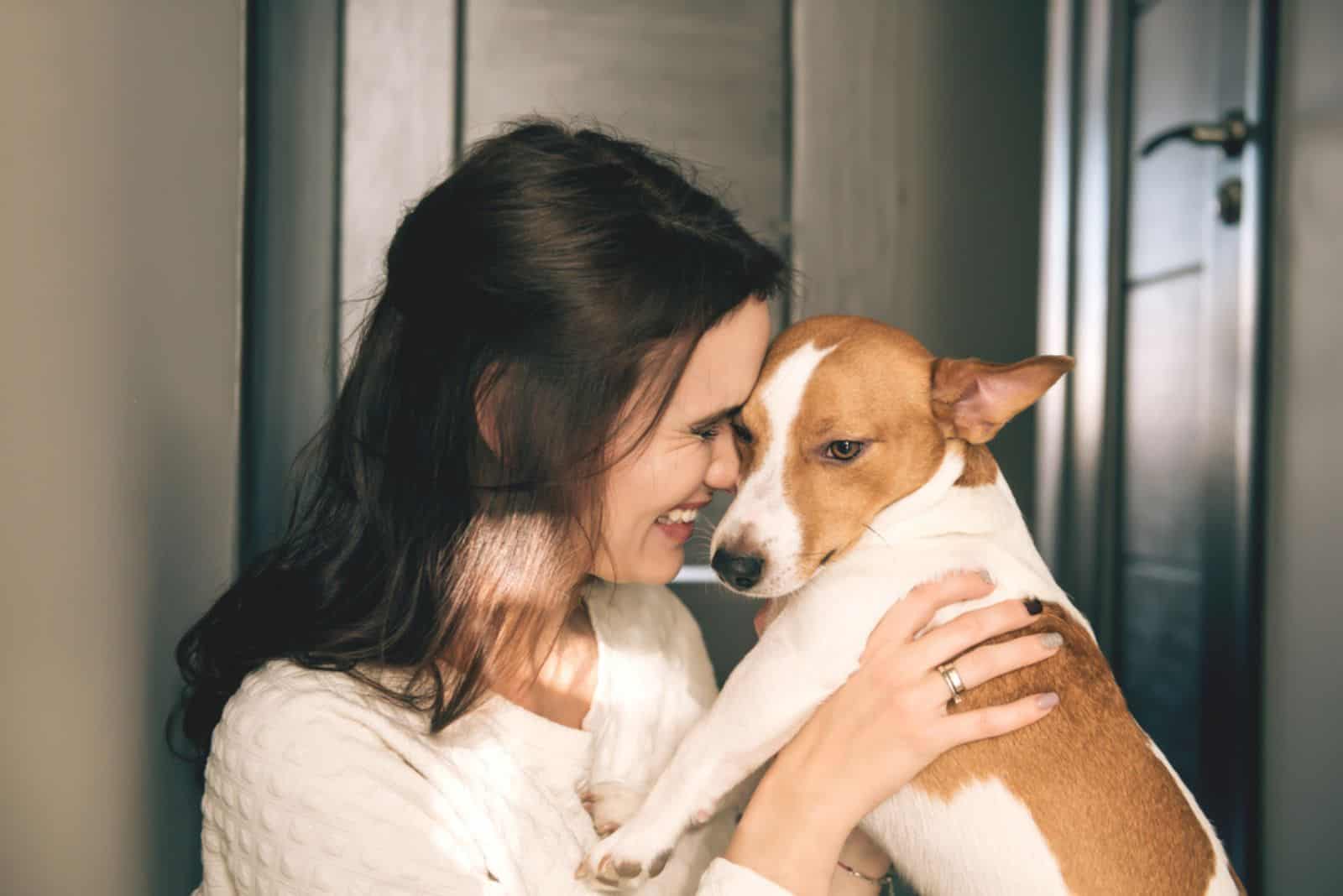 mujer sonriente abrazando a un perro en casa