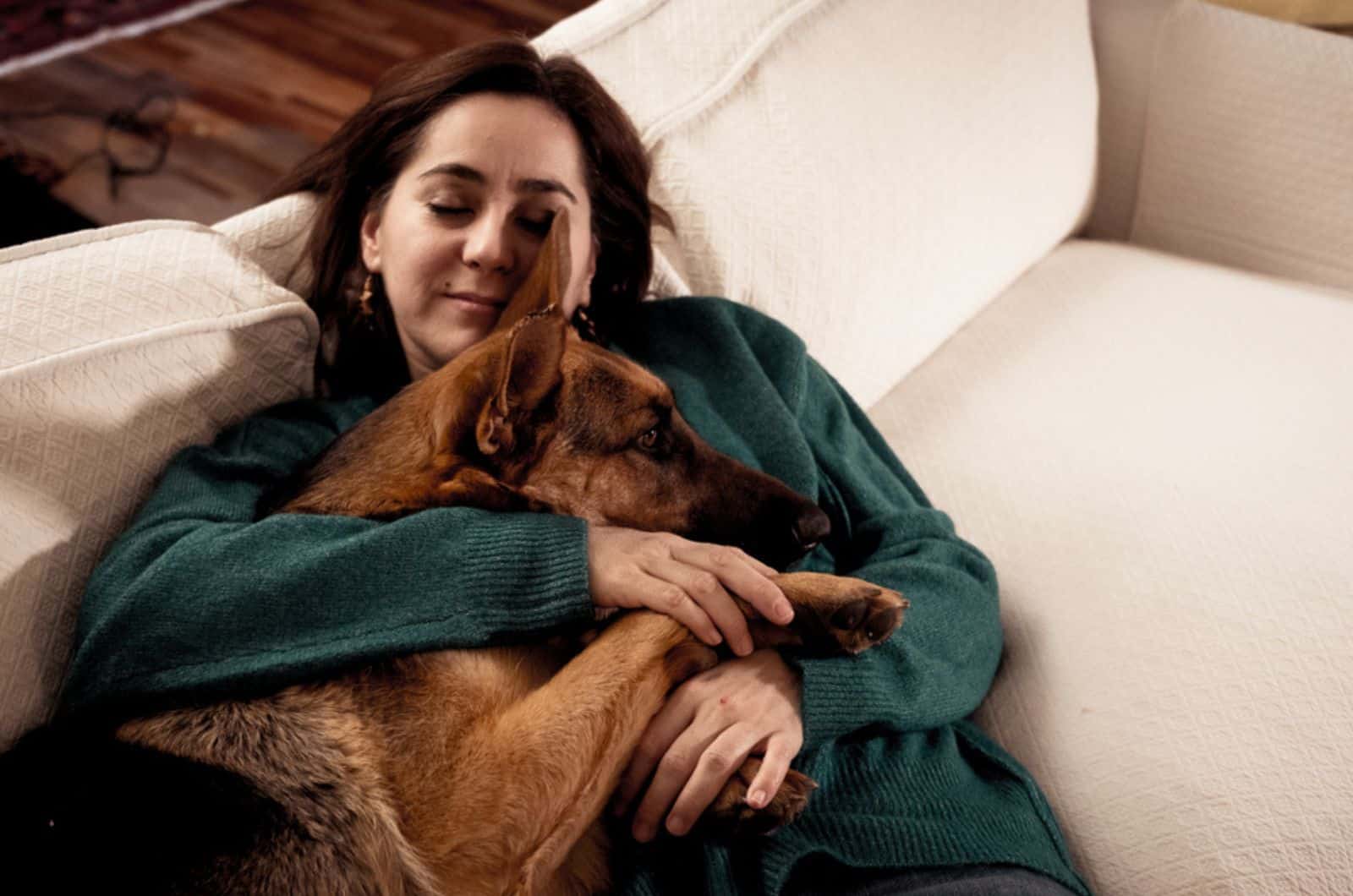 mujer abrazando a su perro pastor alemán en el sofá