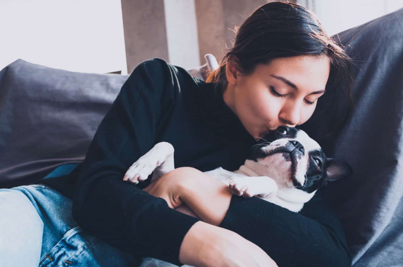 mujer besando a su perro boston terrier en el sofá