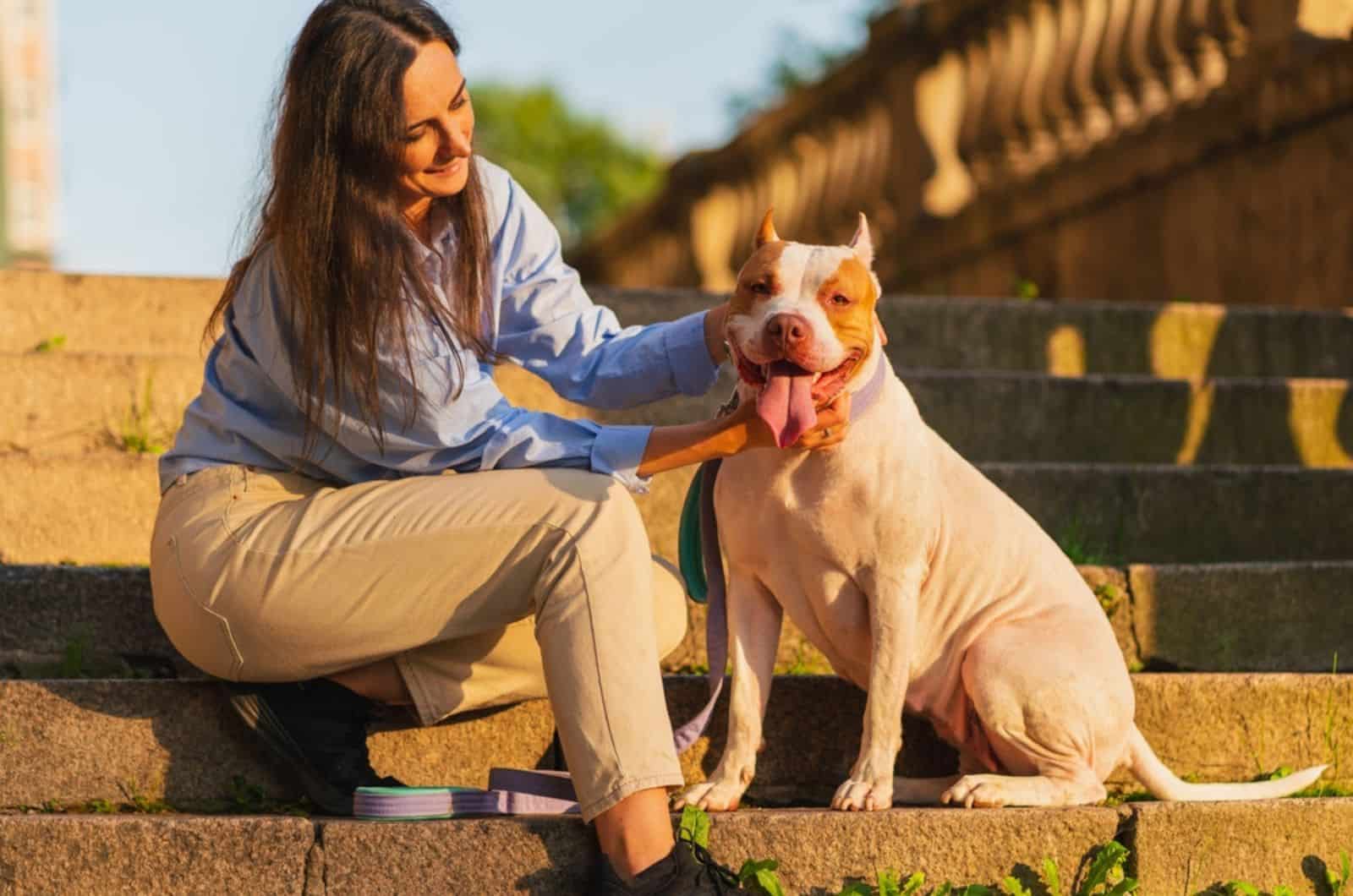 mujer acariciando perro american pitbull terrier mientras está sentada en escaleras de piedra