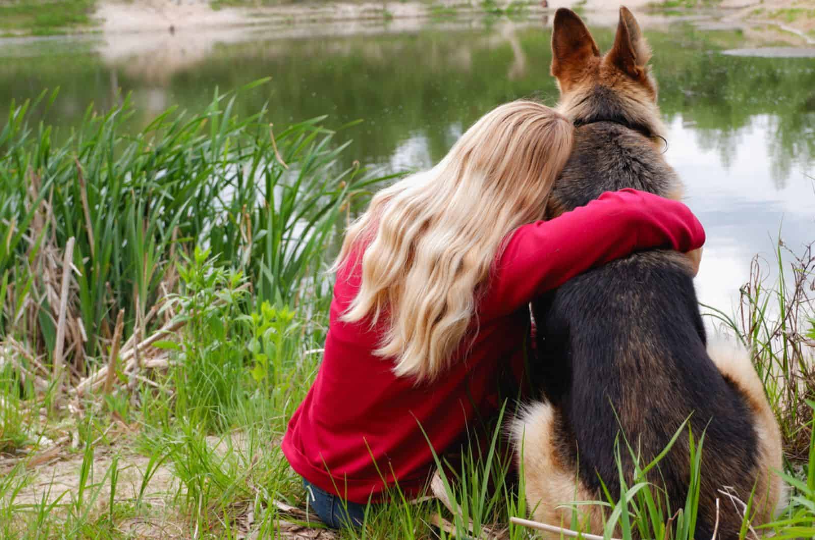 mujer con un perro pastor alemán sentada a la orilla del lago